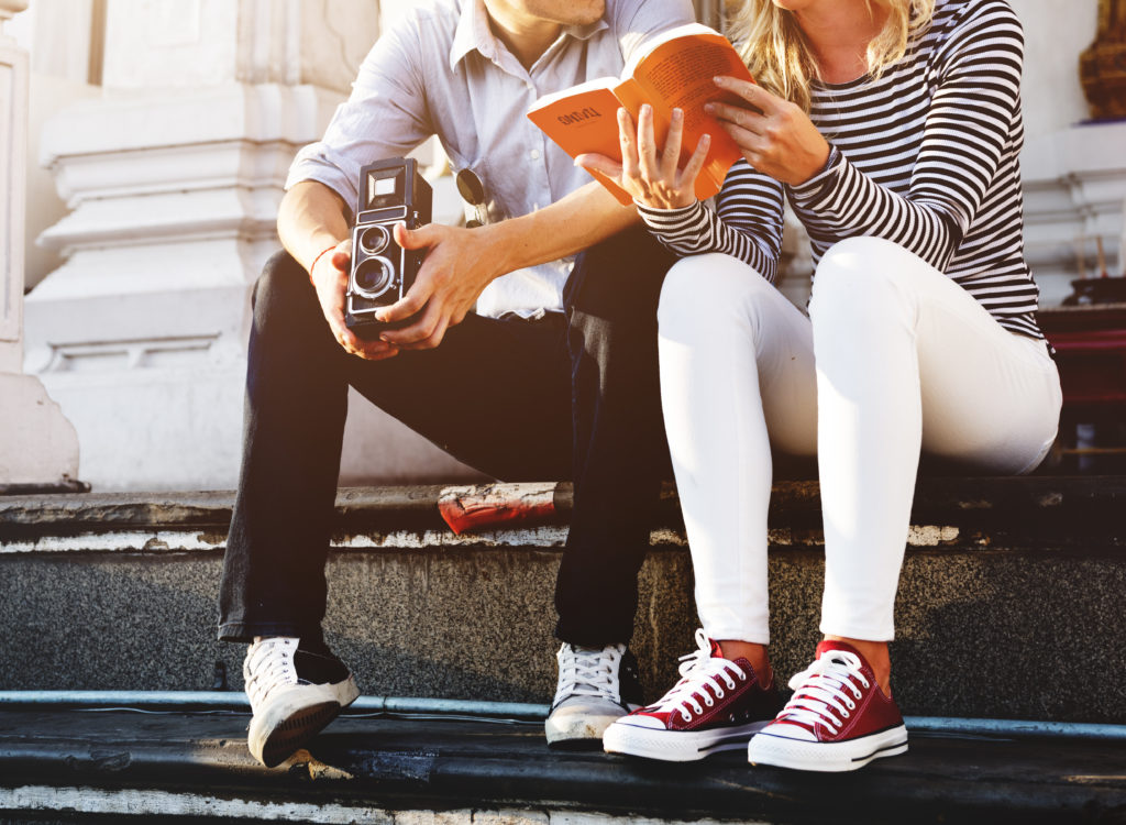 Young girl holding a book open for the guy next to her to see and read for himself. 