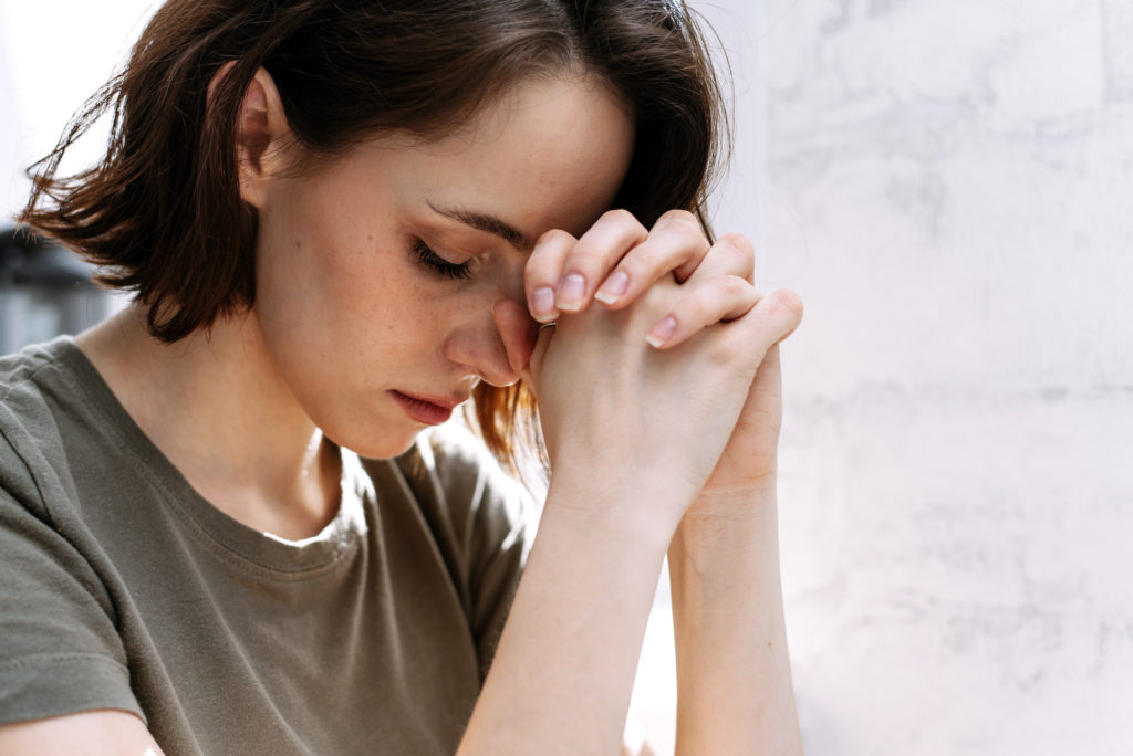 a young woman praying with her hands clasped tight 