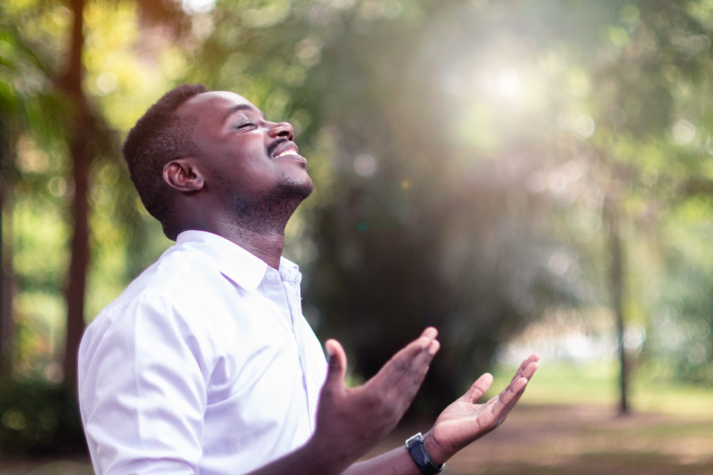 young man standing outside and holding his hands out in prayer as he joyously basks in the presence of God