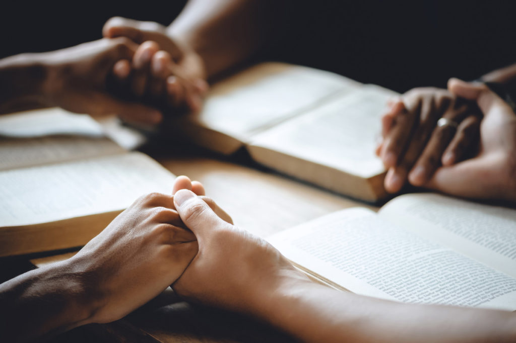 Three people holding hands over their bibles during worship in Johnson City.